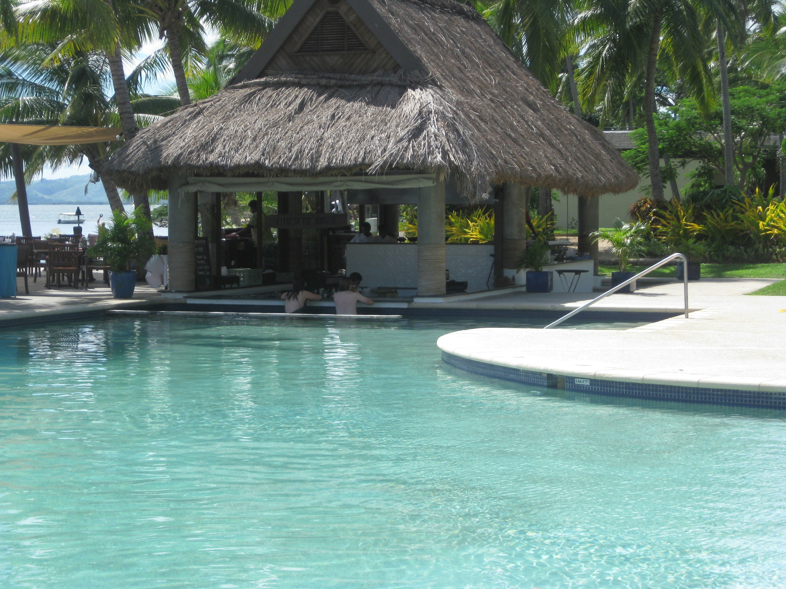 Swim-up bar at tropical resort pool, colorful cocktails on bar counter, guests in water, vibrant atmosphere