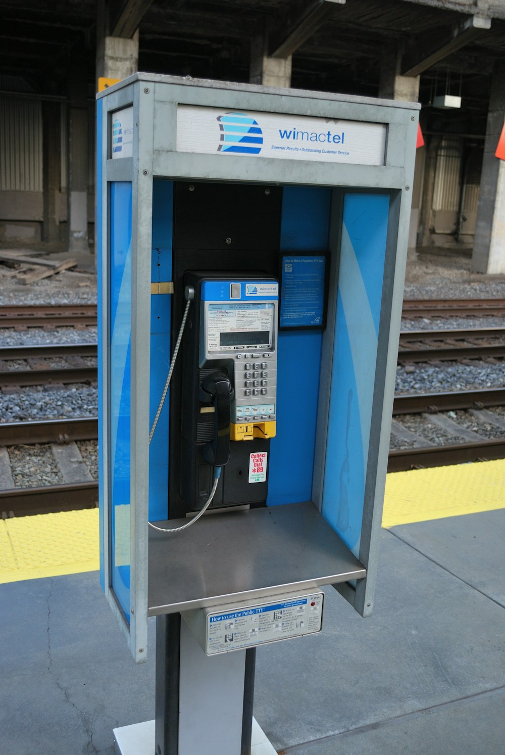 a pay phone sitting on top of a stand next to a train track