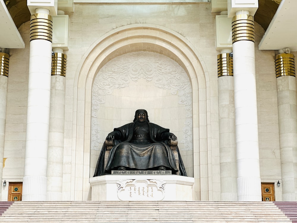 a statue of a man sitting on a bench in front of a building