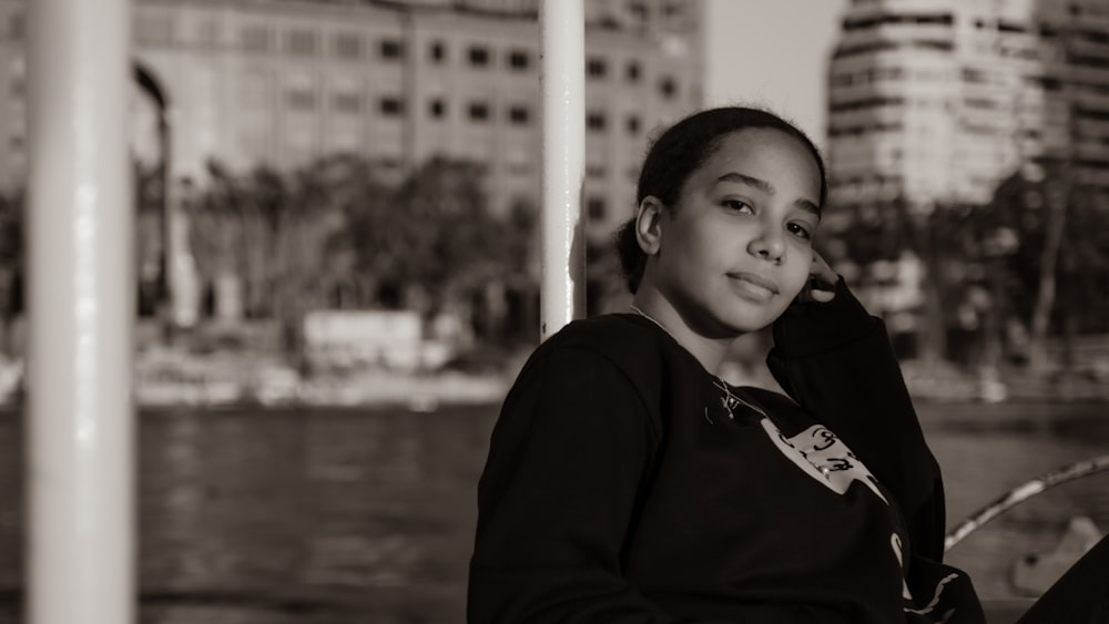 a young girl sitting on a bench in front of a body of water