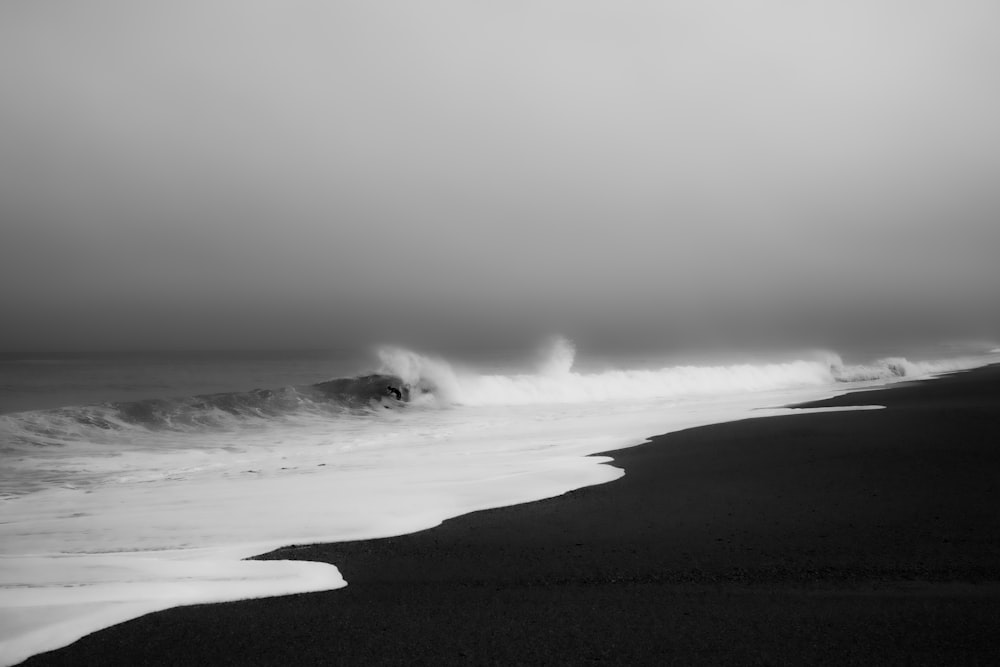 a black and white photo of a wave crashing on the beach
