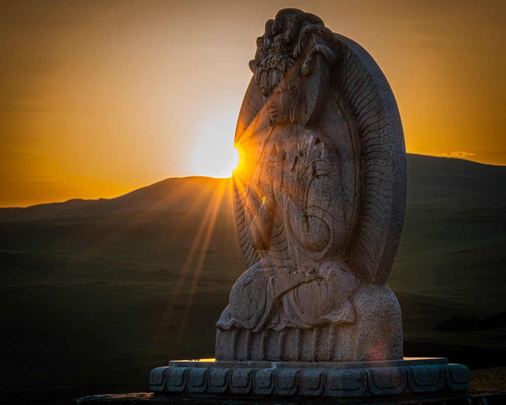 a statue with the sun setting behind it