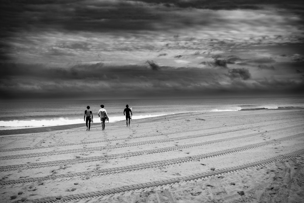 three surfers are walking along the beach under a cloudy sky
