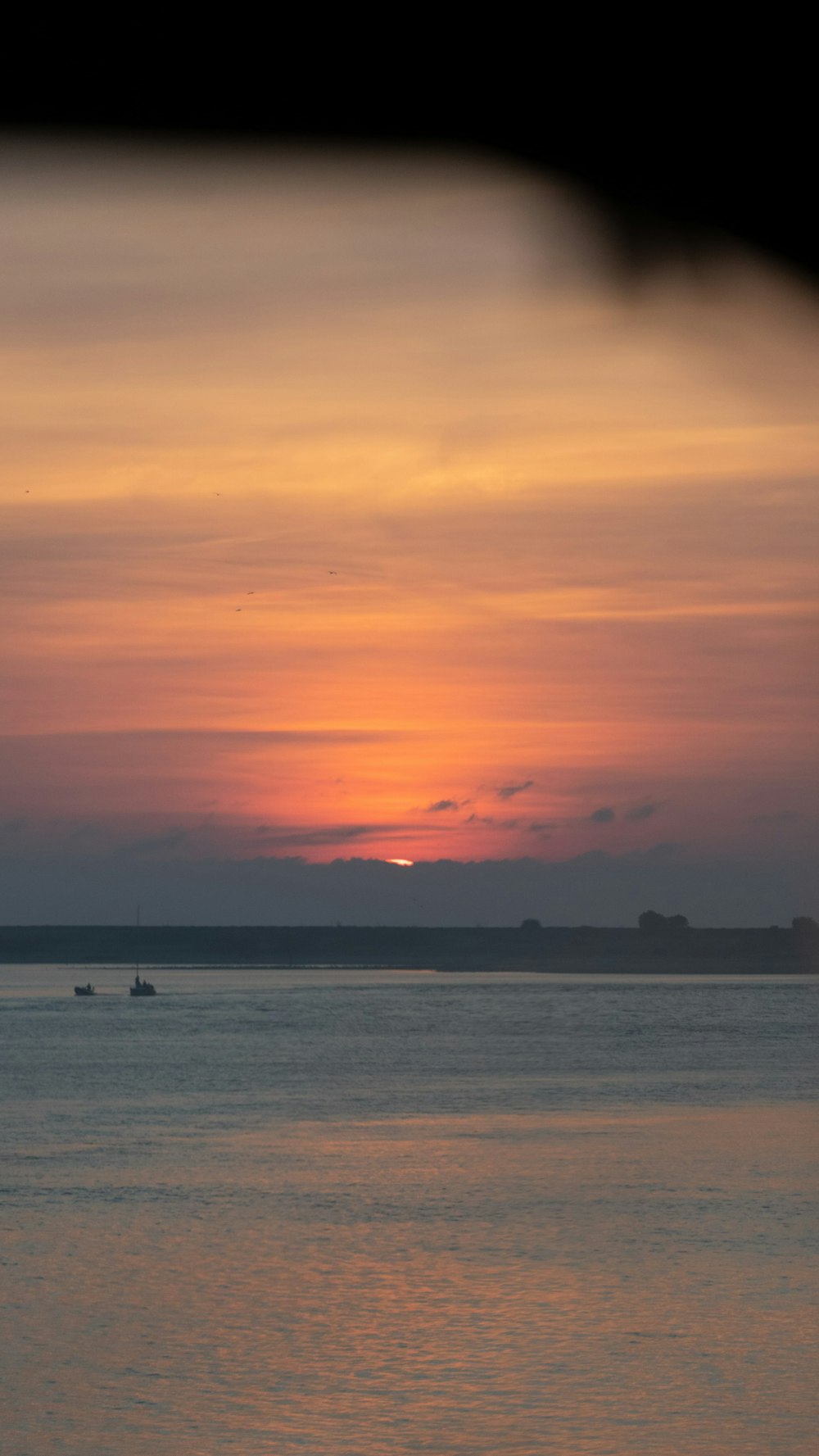 a sunset over a body of water with a boat in the distance