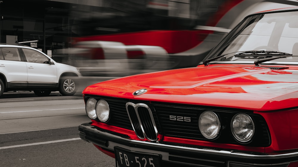 Un coche rojo circulando por una calle junto a un coche blanco