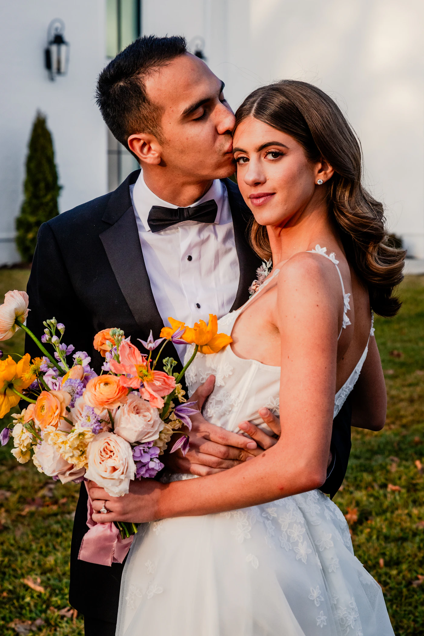 Couple in wedding attire kissing in front of a historic stone building