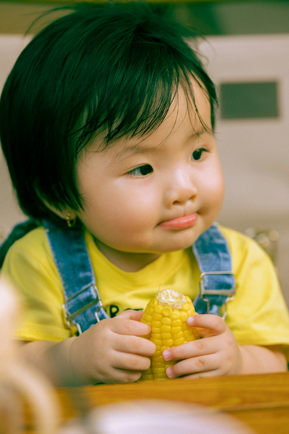 a young child sitting at a table eating a corn on the cob