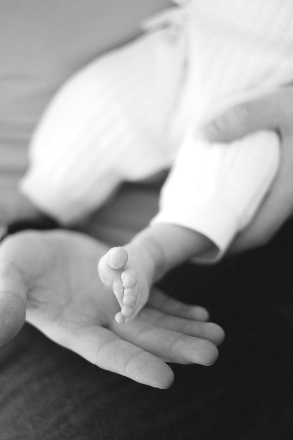 a black and white photo of a person holding a baby's hand