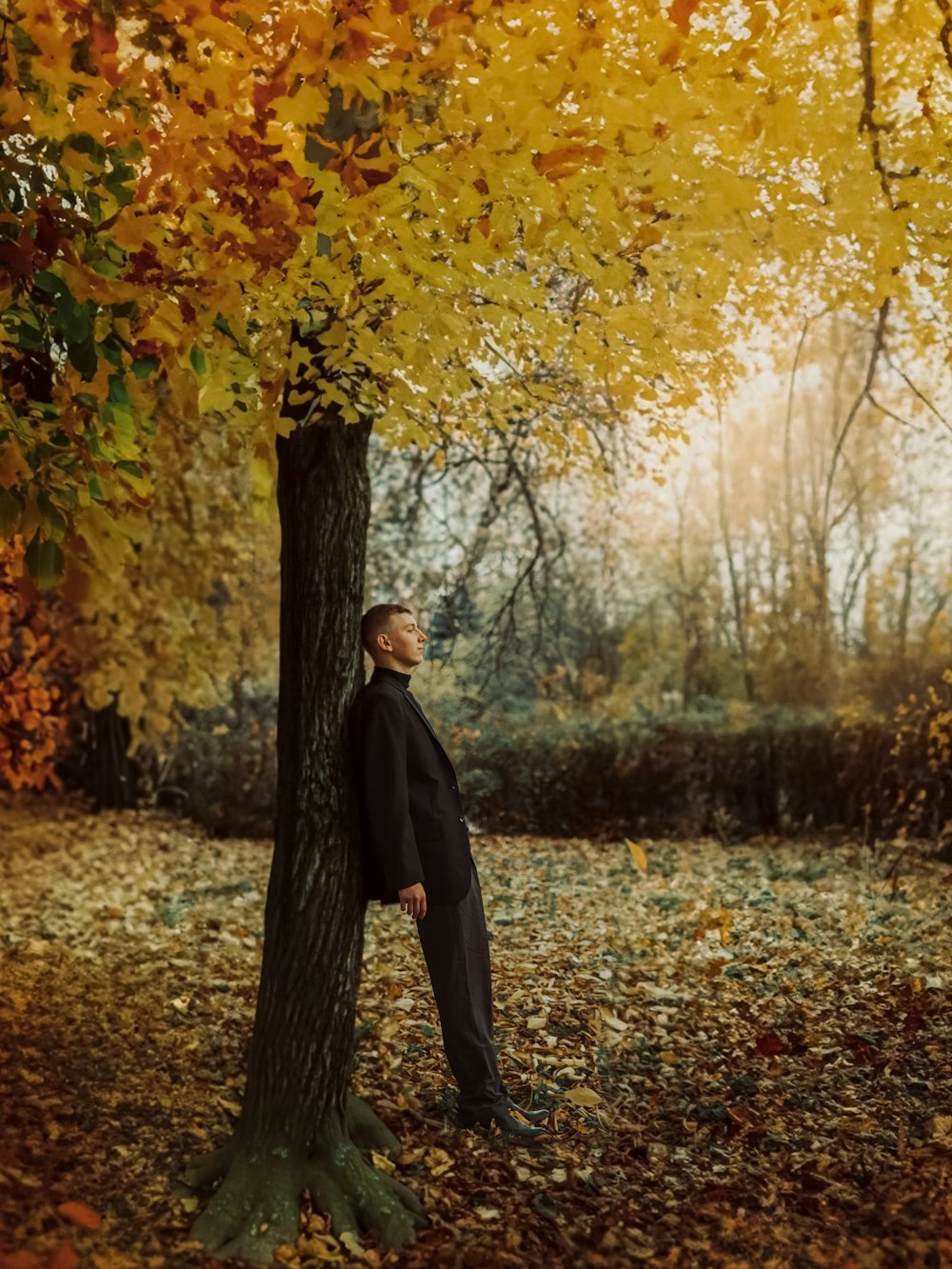 a man in a suit leaning against a tree