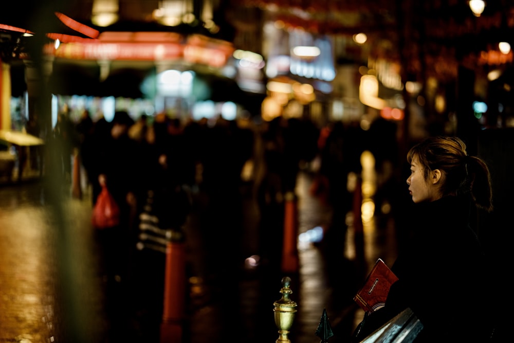 a woman sitting on a bench in a city at night