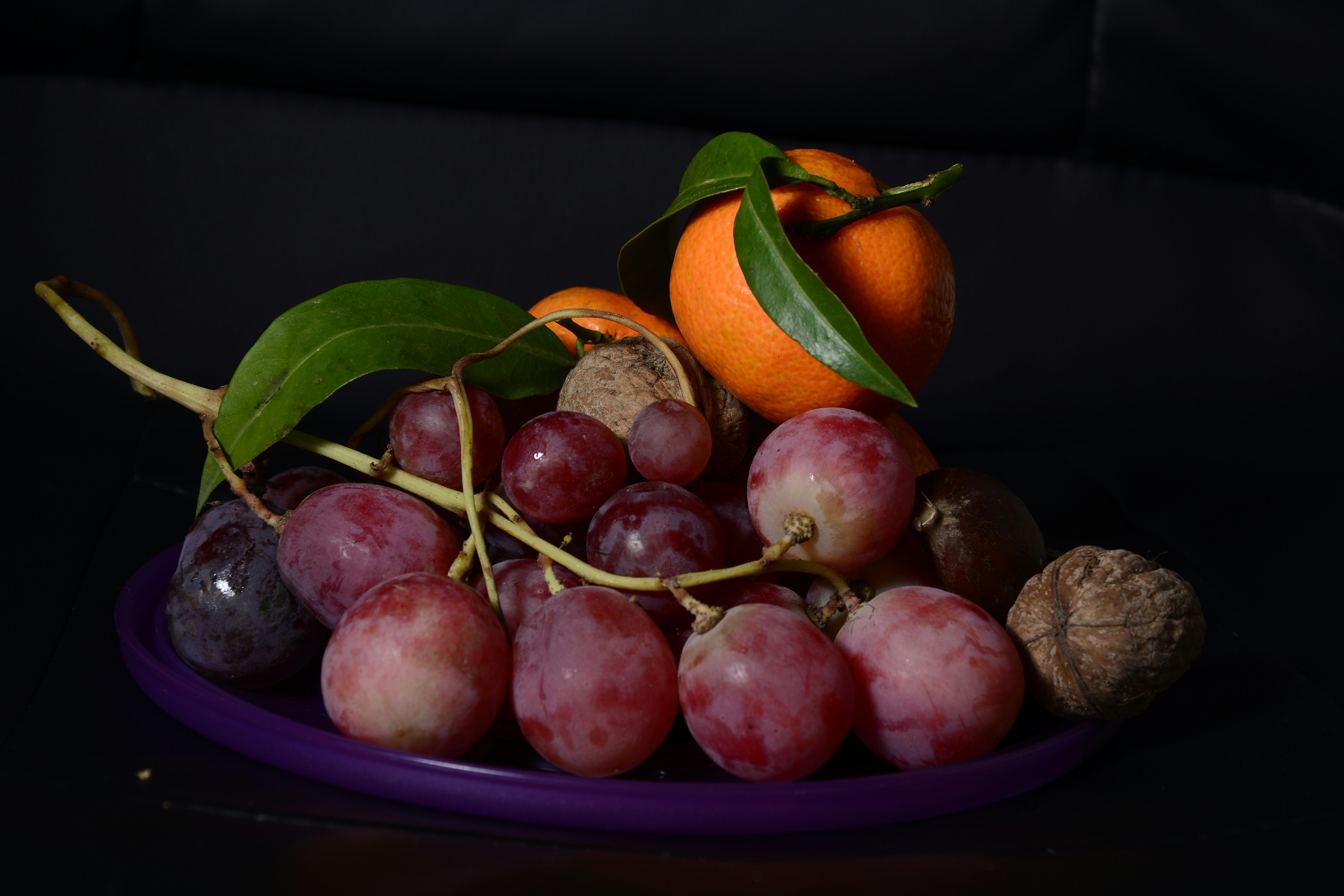 une assiette de raisins, de noix et une orange sur une table