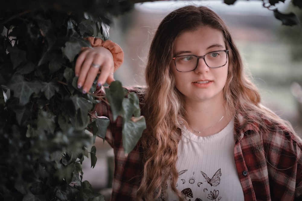 a young girl wearing glasses standing next to a tree