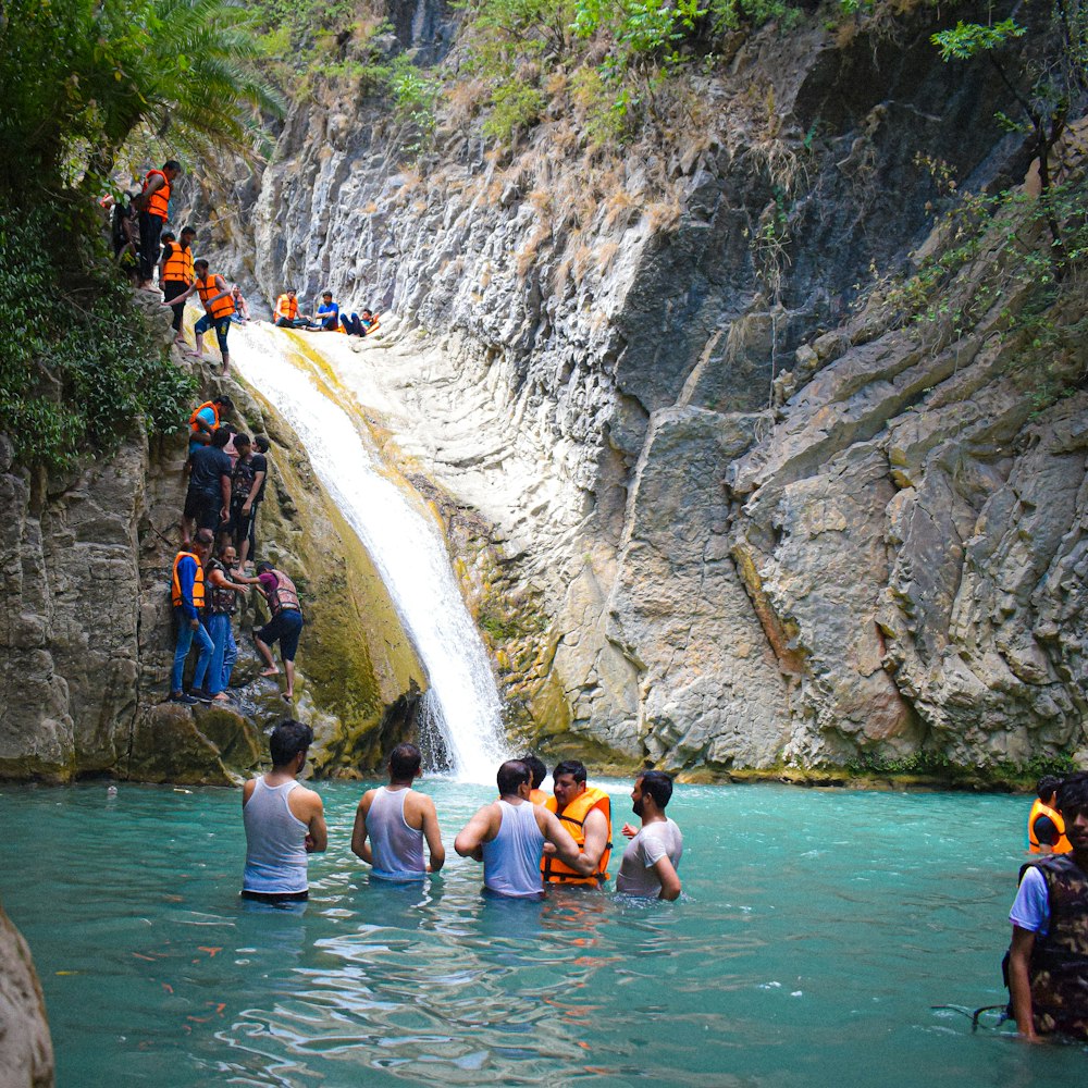 a group of people standing in the water near a waterfall