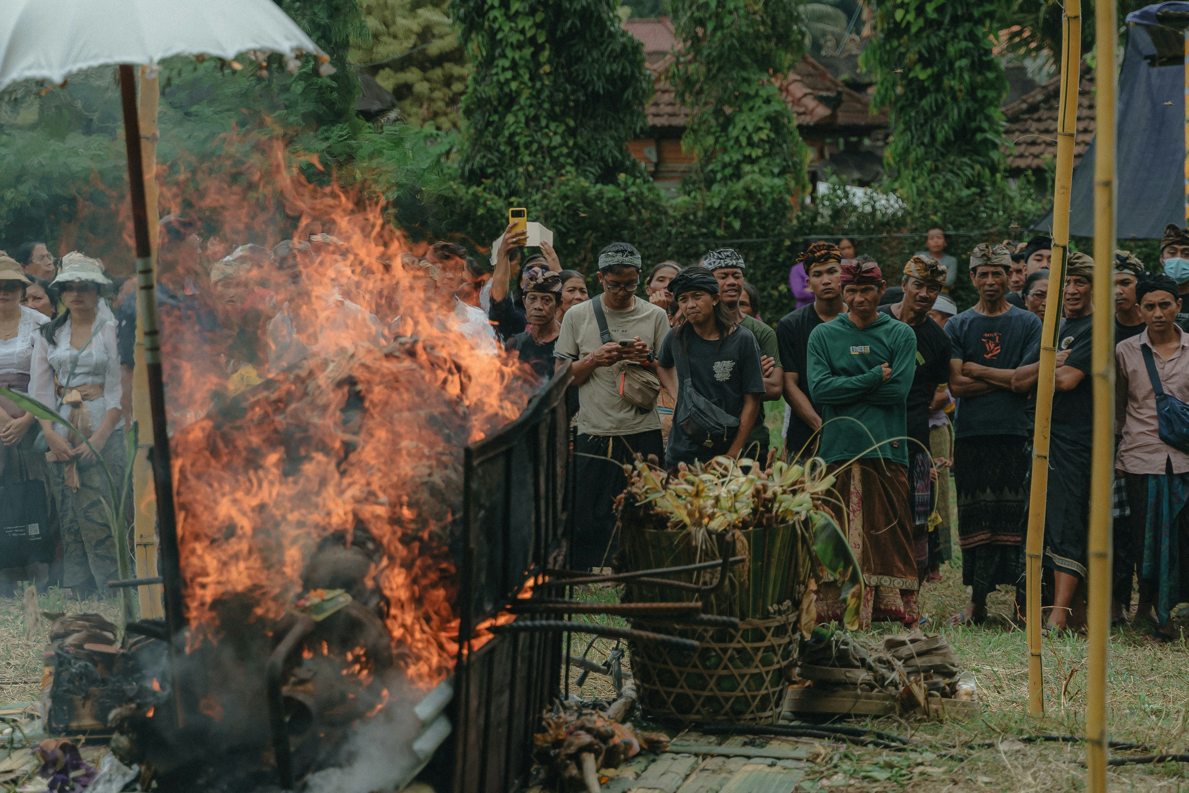 a group of people standing around a fire pit, The cremation procession in Bali, known as Ngaben, is surrounded and witnessed by people