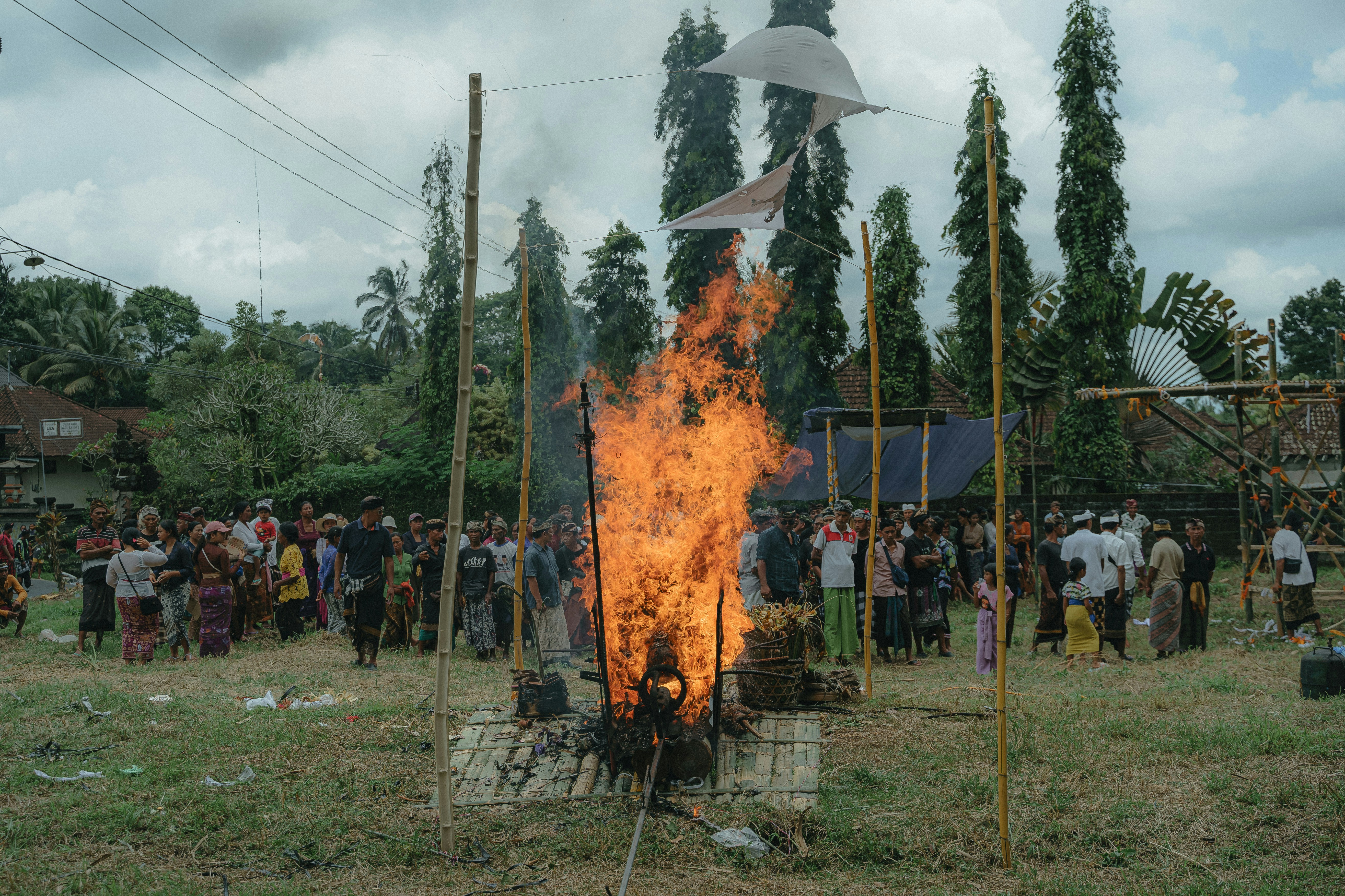 a group of people standing around a fire, The cremation procession in Bali, known as Ngaben, is surrounded and witnessed by people