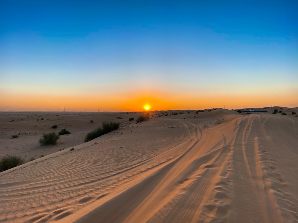 the sun is setting over the desert with tracks in the sand