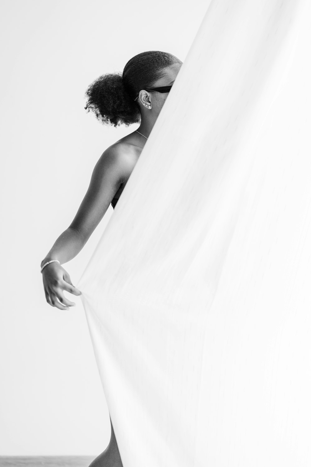 a black and white photo of a woman hiding behind a curtain