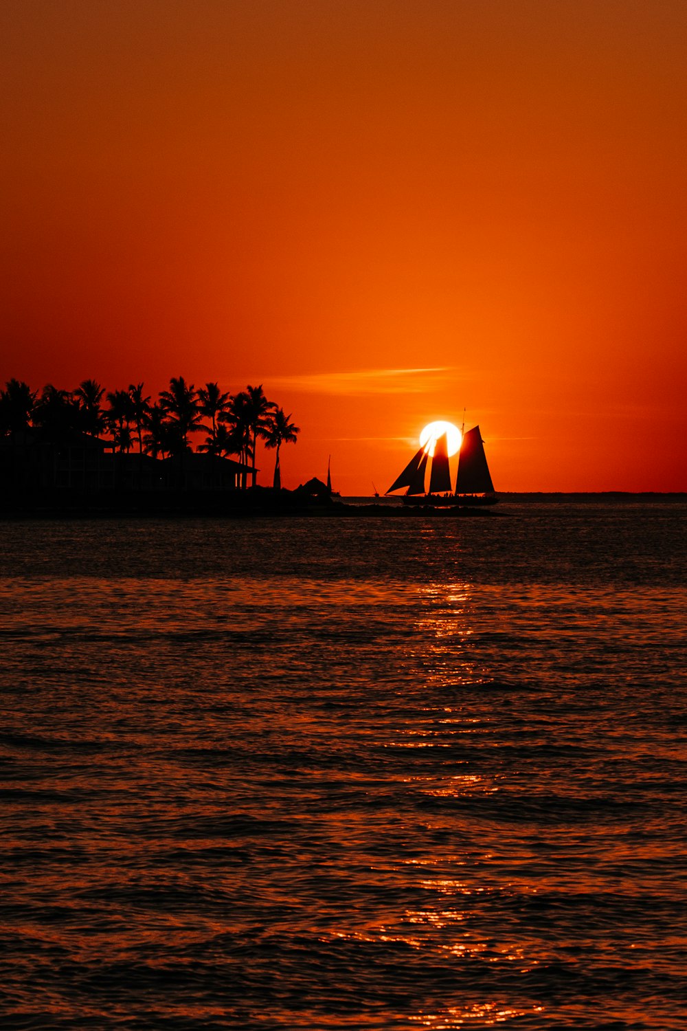 the sun is setting over the ocean with a sailboat in the foreground