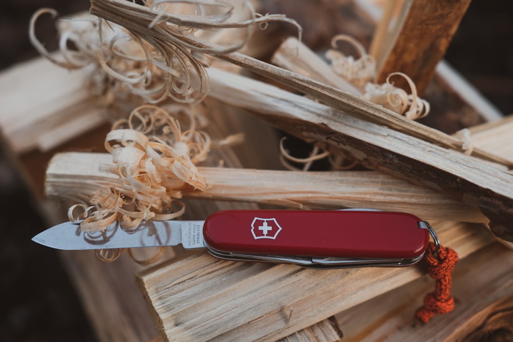 a red pocket knife sitting on top of a pile of wood