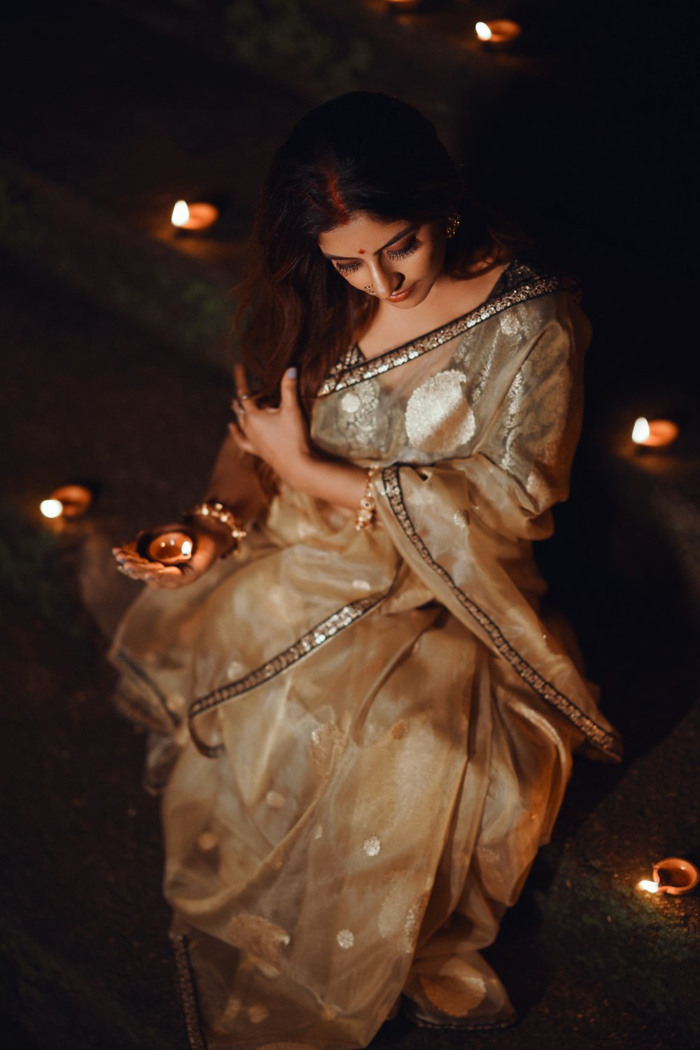 a woman in a gold sari holding a lit candle