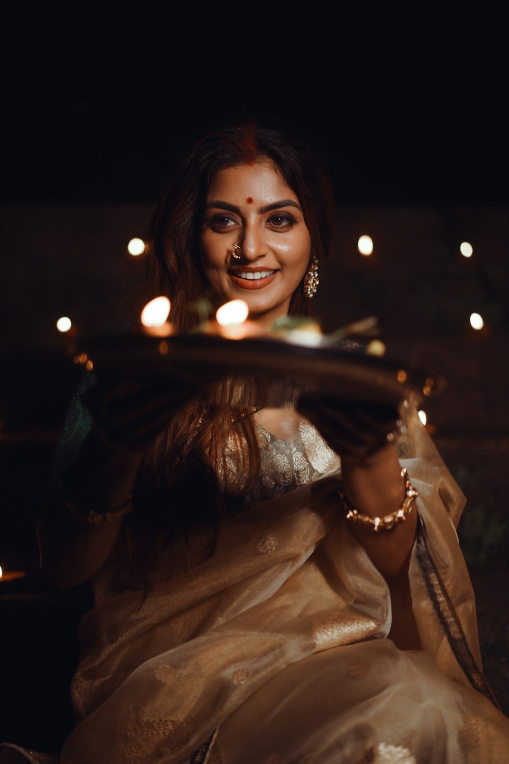 a woman in a sari holding a tray with candles on it