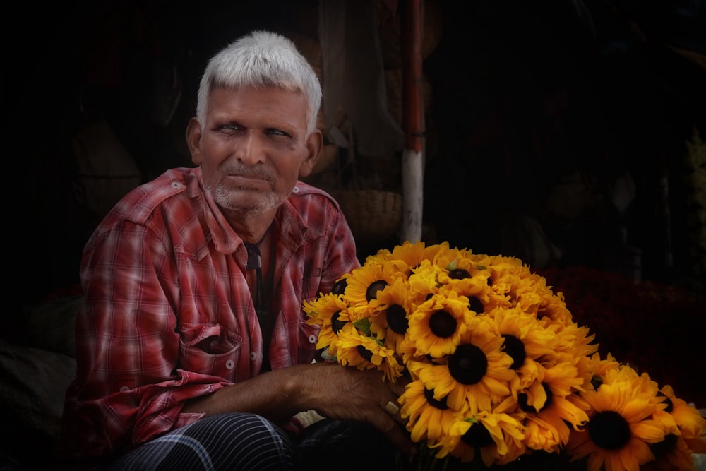 a man sitting next to a bunch of sunflowers