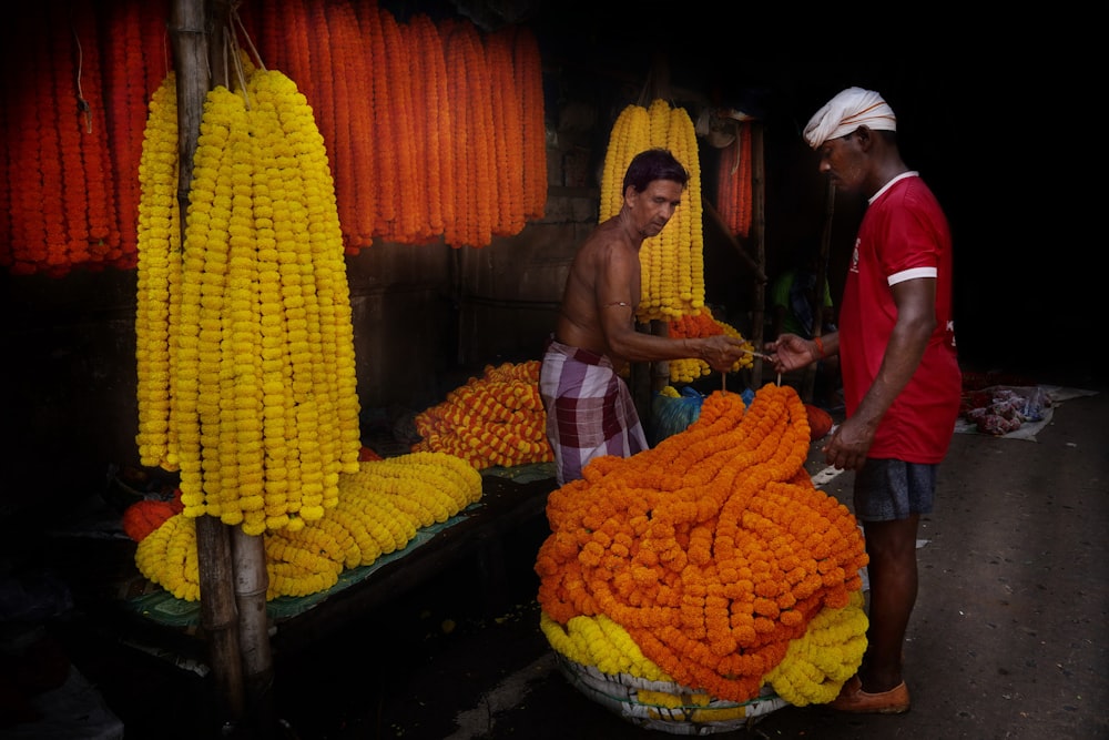 a couple of men standing next to a pile of corn