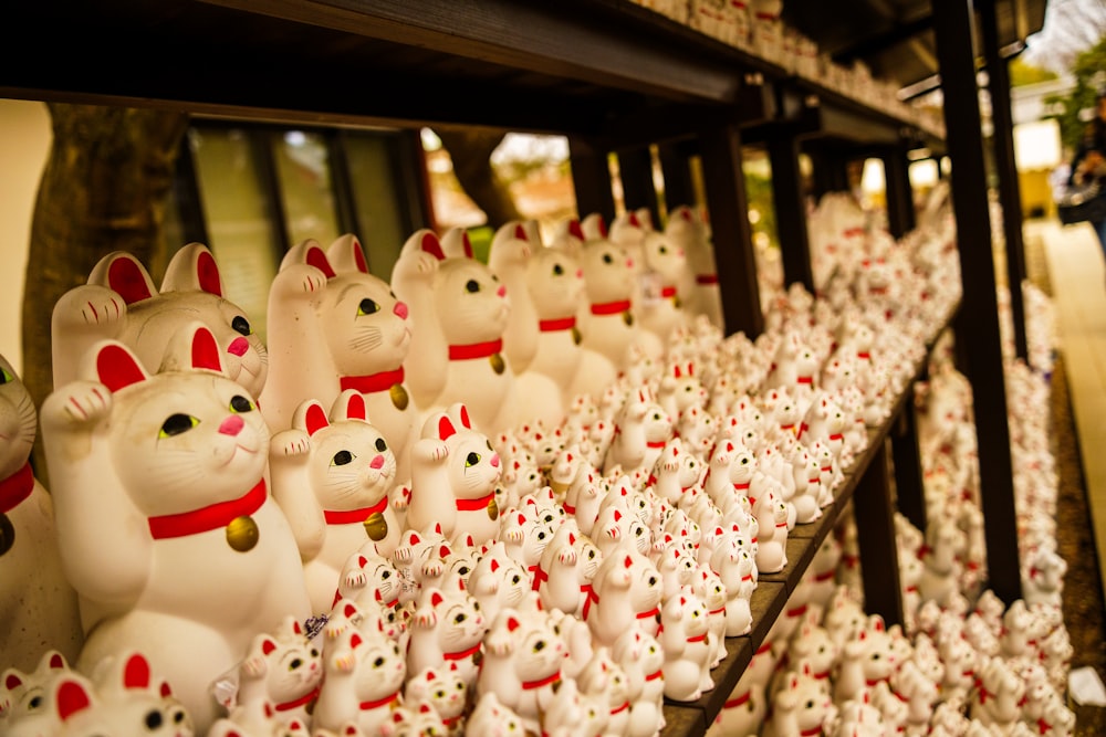 a row of white cat figurines sitting on top of a shelf