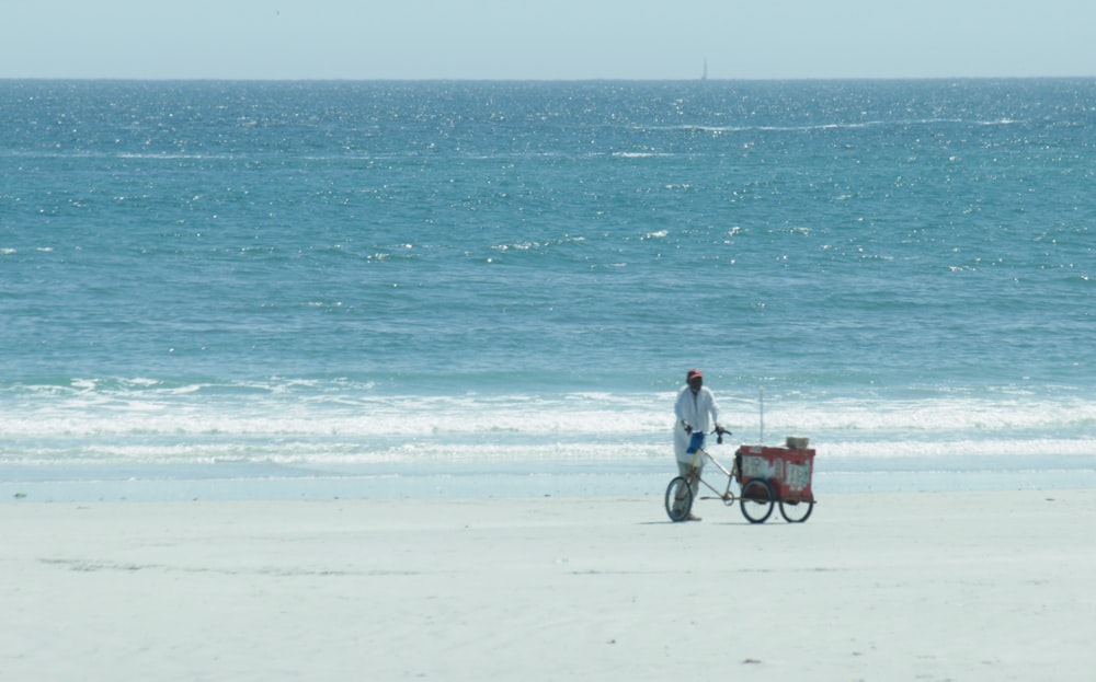 um homem em uma praia puxando um carrinho com uma prancha de surf