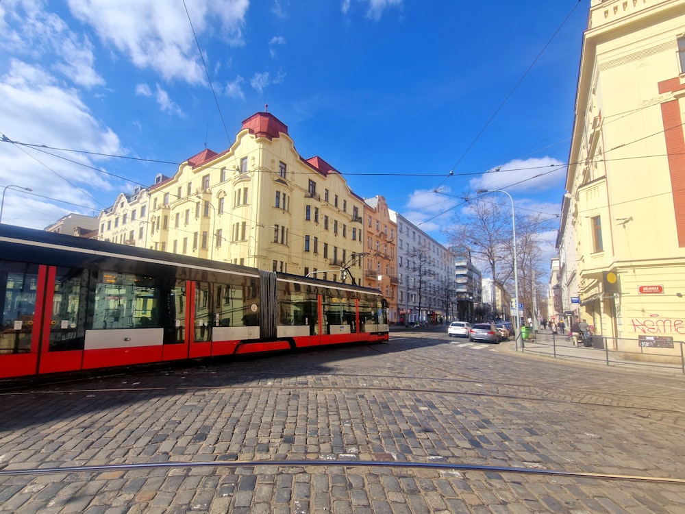 a red and white train traveling down a street next to tall buildings