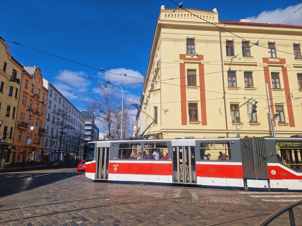 a red and white train traveling down a street next to tall buildings