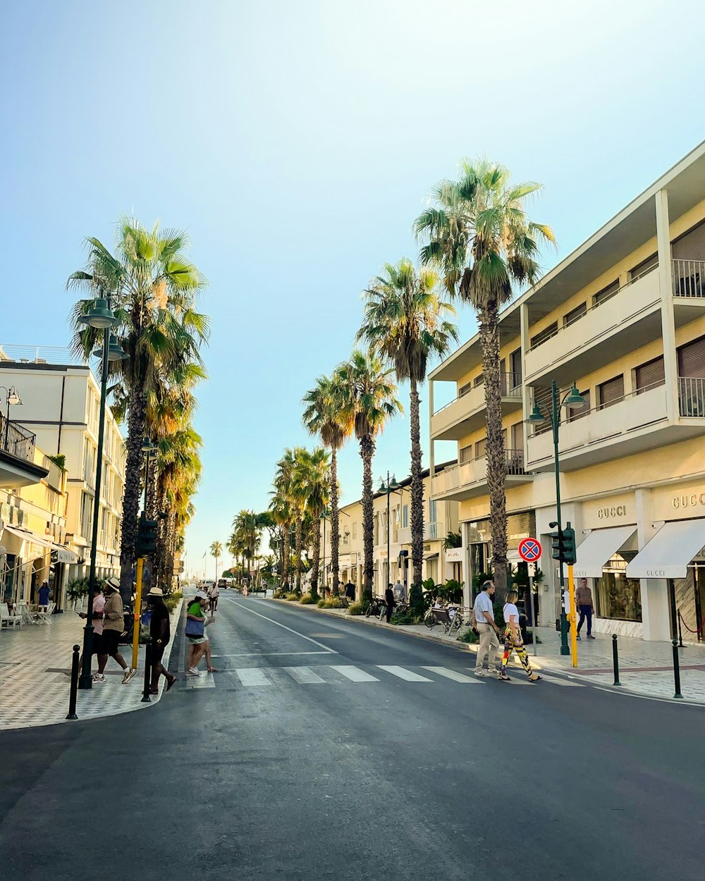 a group of people walking down a street next to palm trees