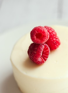 three raspberries on top of a white cake