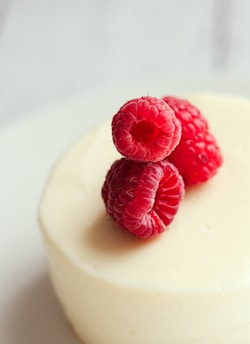 three raspberries on top of a white cake