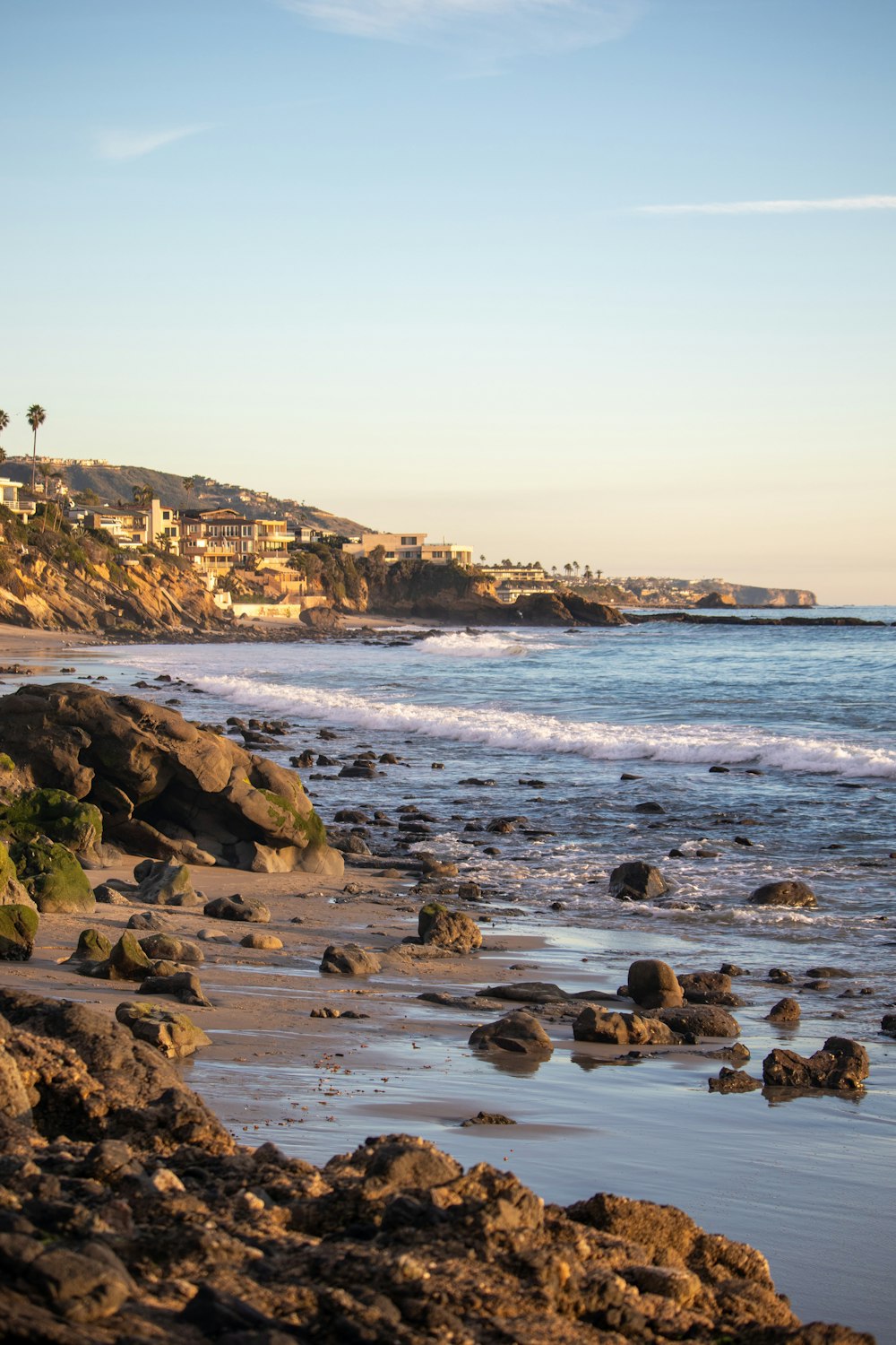 a view of a beach with rocks and houses in the background