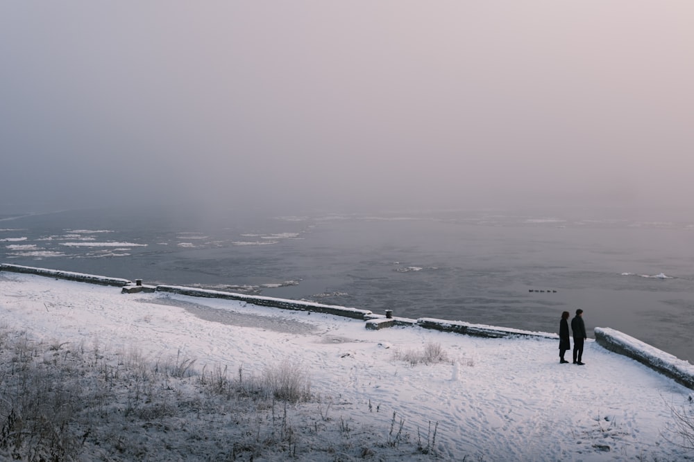 Un par de personas de pie en la cima de una ladera cubierta de nieve
