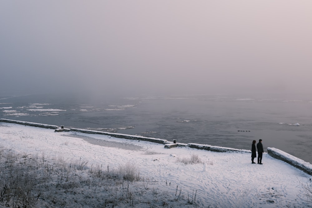 a couple of people standing on top of a snow covered slope