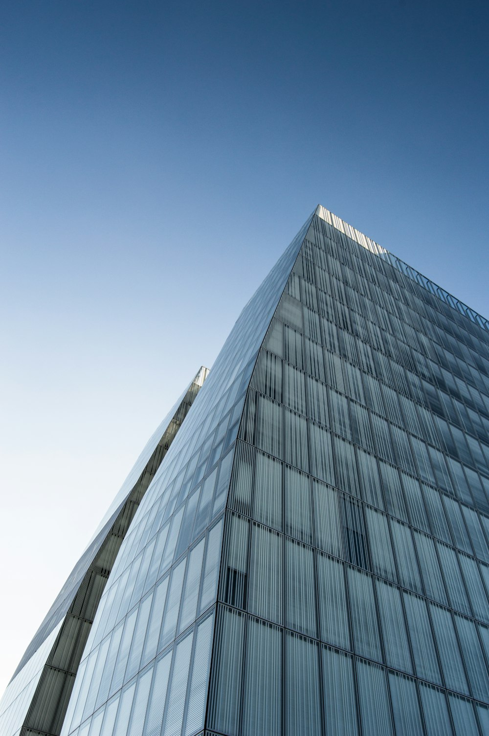 Un edificio di vetro molto alto con uno sfondo di cielo