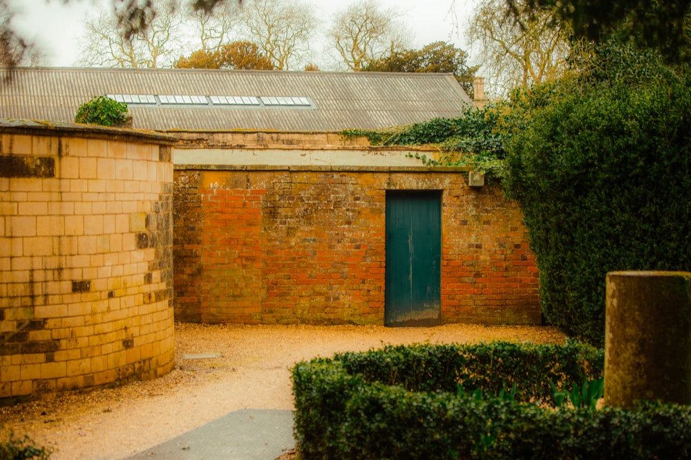 a brick building with a green door surrounded by hedges