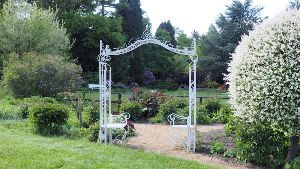a garden with a white bench and a white arbor