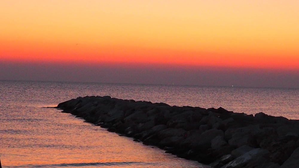 a person standing on a rocky shore watching the sun set