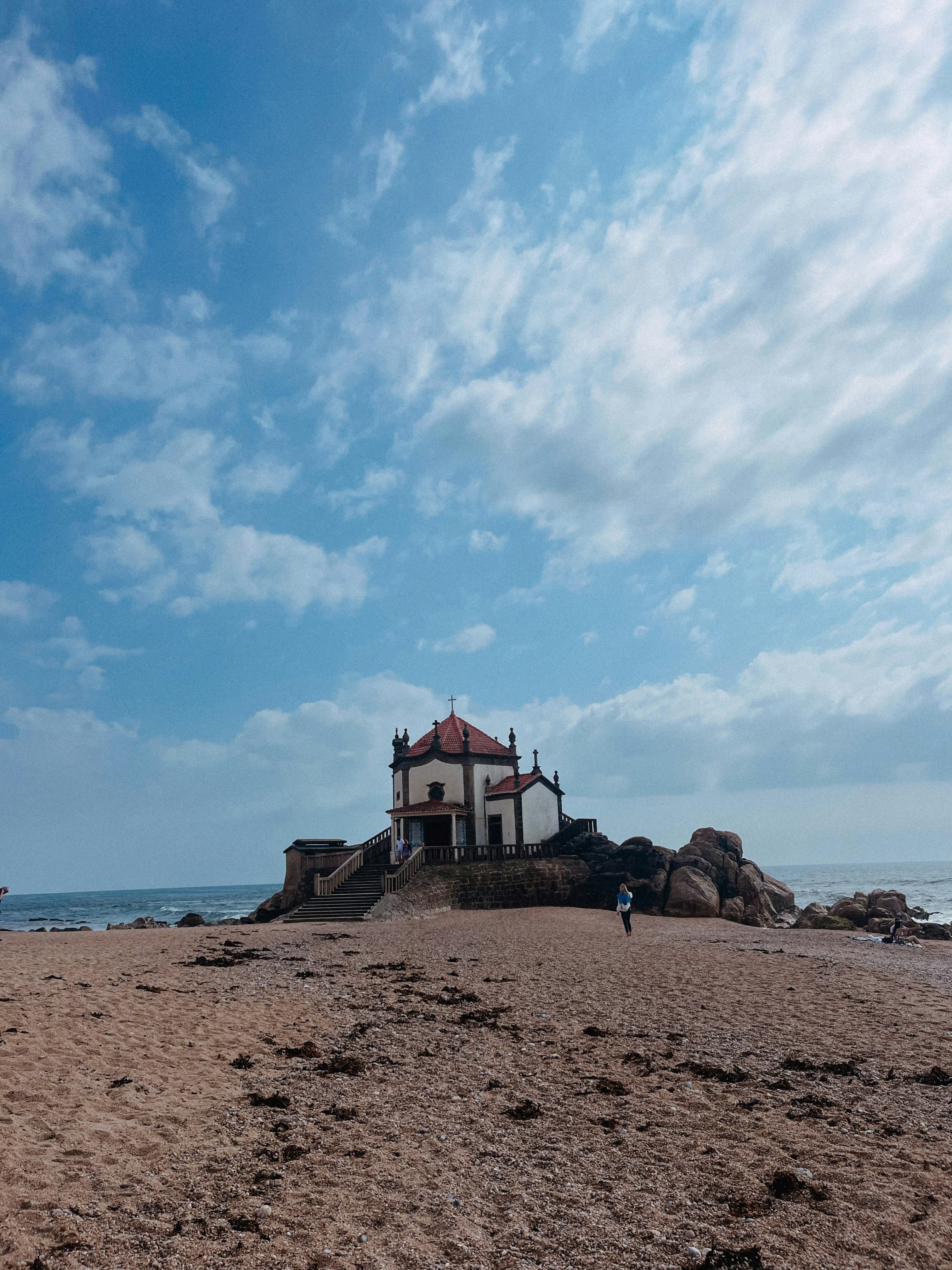 a small white and red building on a sandy beach