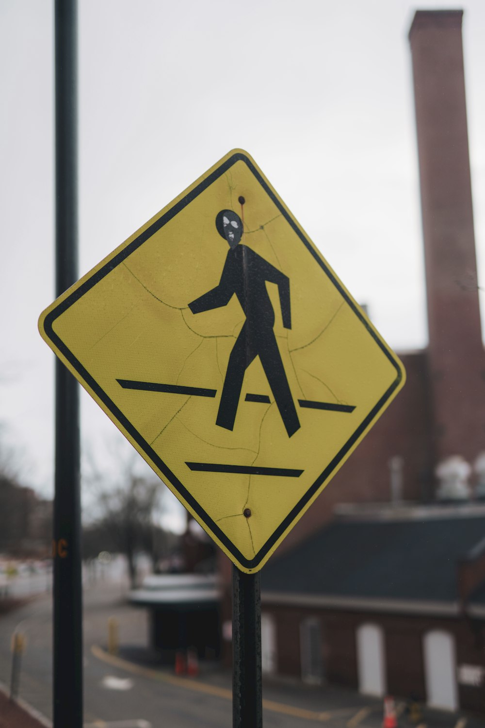 a yellow pedestrian crossing sign sitting on the side of a road