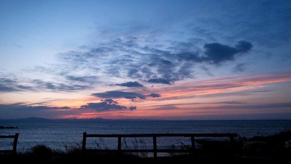 a sunset over a body of water with a fence in the foreground