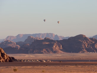two hot air balloons flying over a desert landscape