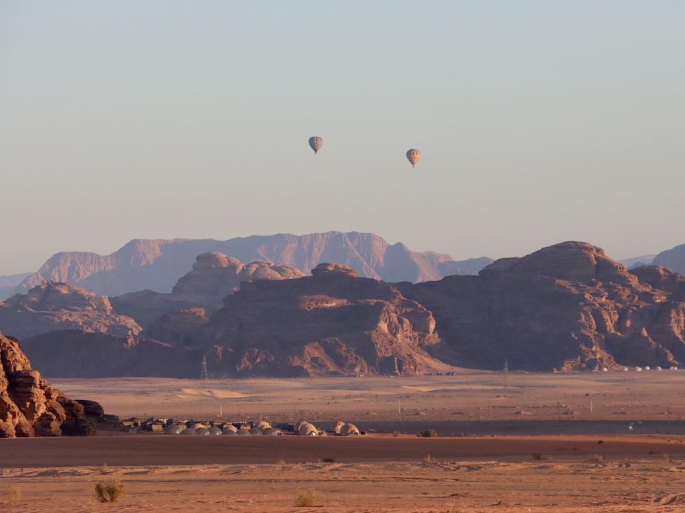 two hot air balloons flying over a desert landscape