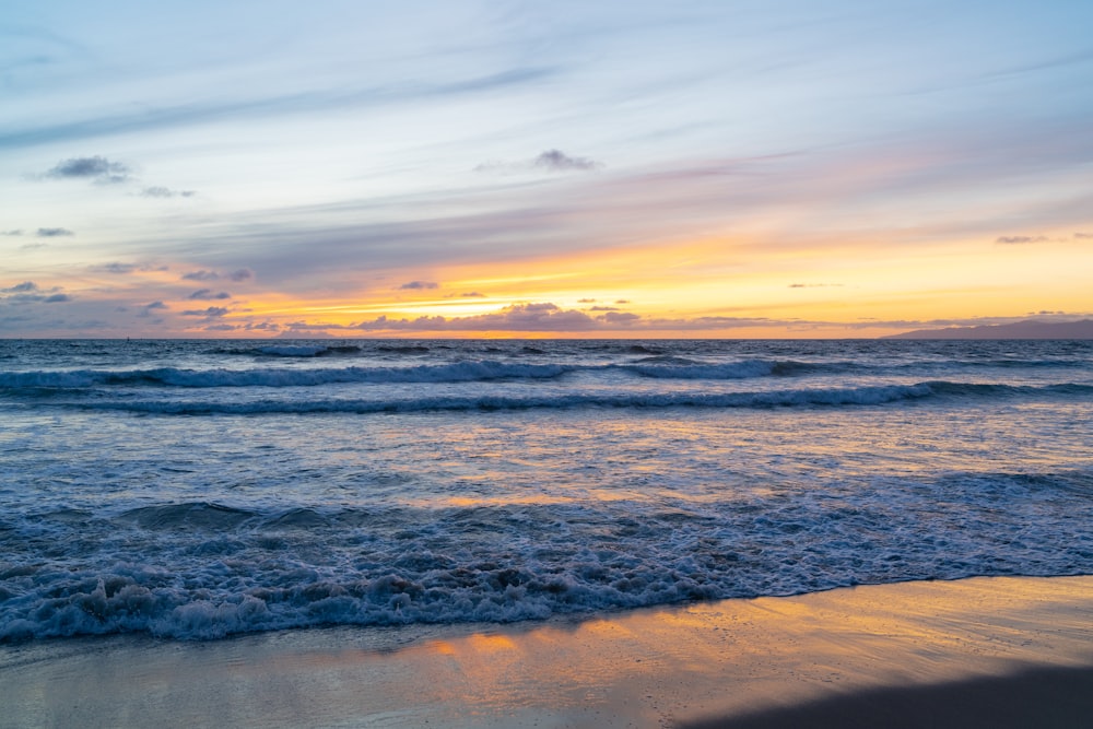 a sunset over the ocean with waves coming in