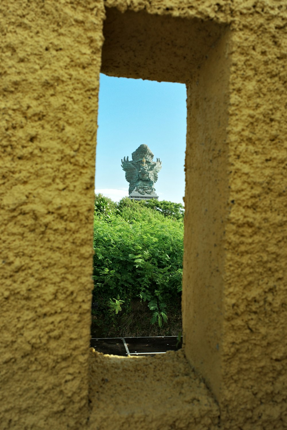 uma vista de uma estátua através de um buraco em uma parede
