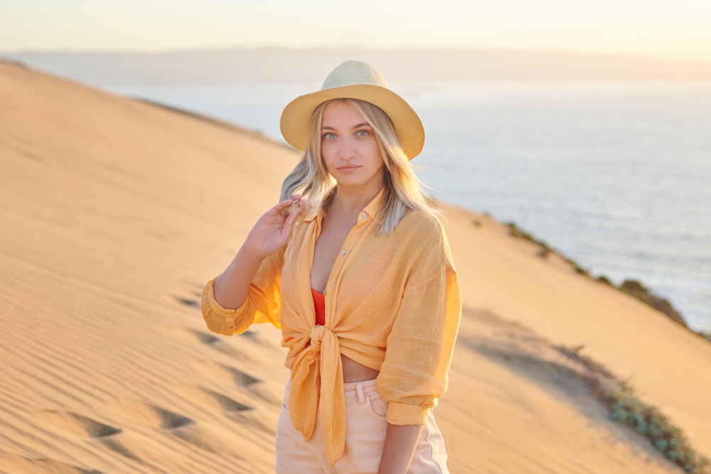 uma mulher de camisa amarela e chapéu em pé na areia