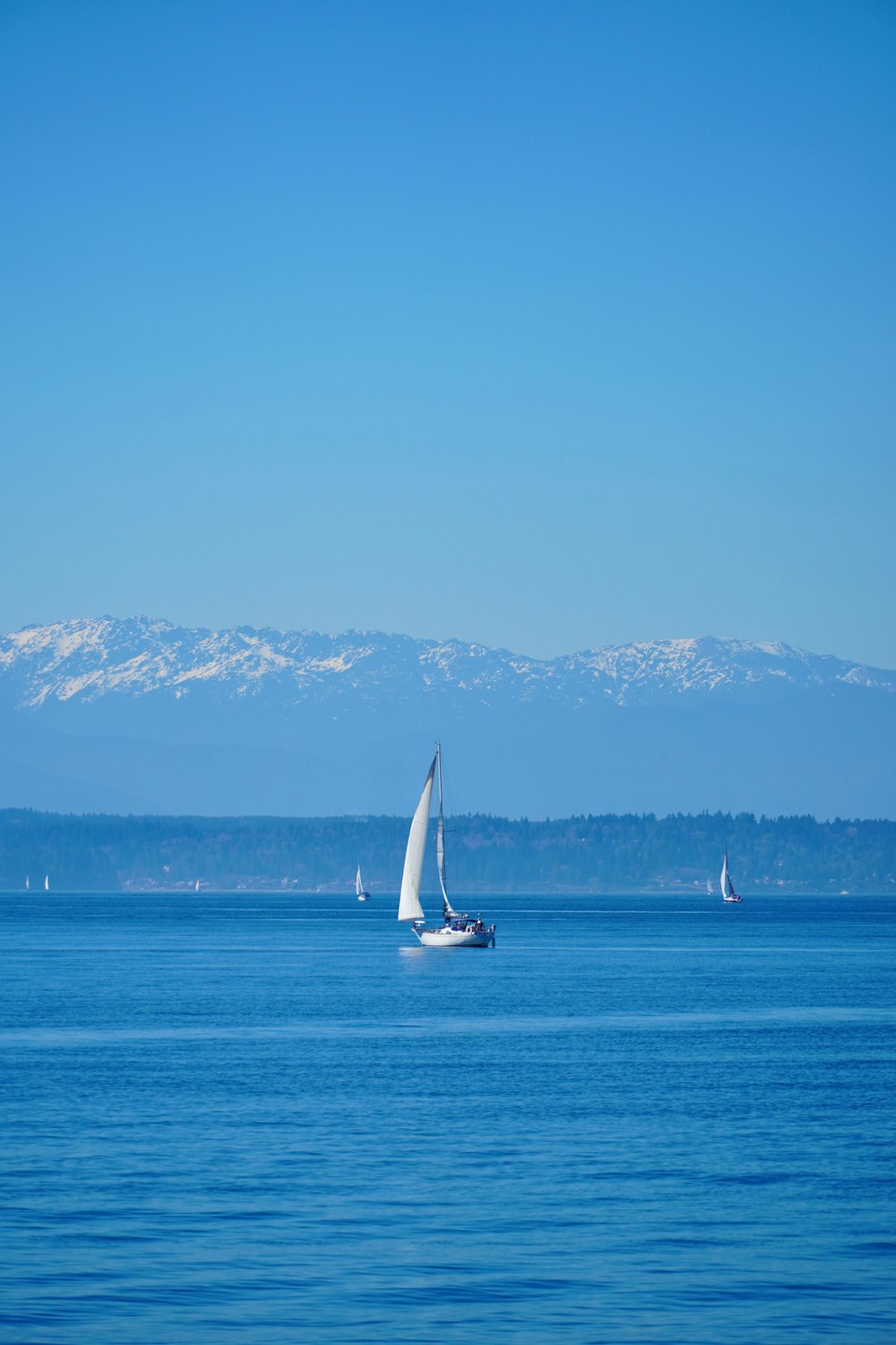 a sailboat in the middle of the ocean with mountains in the background